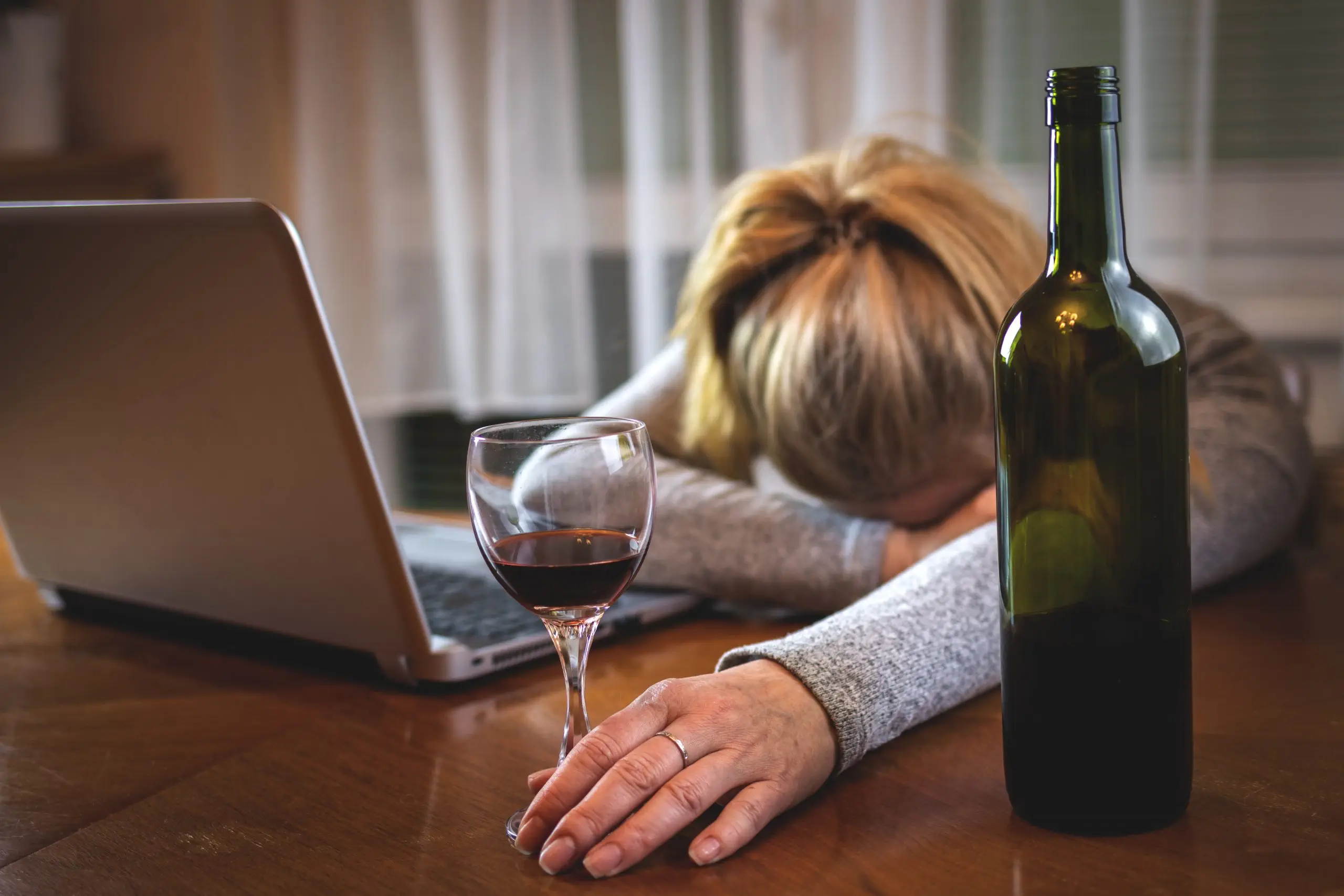 Drunk woman with open laptop sleeping on table after drinking red wine